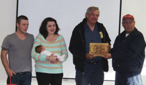Phil Mass of Family Automotive in Meeker, right, presented this handmade etched duplicate of a firefighter’s badge to Vaughn Moody on Monday evening at the Meeker fire station. Moody was the first Meeker Fire and Rescue responder to a recent accident south of Meeker, and he helped save Mass’s granddaughter, Brittany, and his then-unborn great-granddaughter, Scarlett, second from left, and Brittany’s husband, Andrew Lawrence, left, who were in an accident on April 17, when the family vehicle slid off Highway 13 and the mother and daughter were trapped in the vehicle below the embankment. The plaque, handmade by grandfather Phil Mass, honors all those responsible for helping at the scene and making certain that no one was injured.
