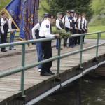While several area residents, members of the Meeker VFW, the Meeker VFW Ladies Auxiliary and the American Legion looked on at 9:30 a.m. Monday, Peter Kiser, left center, tosses a wreath into the White River with the help of auxiliary member Dawn Jastrem. The wreath honors Meeker-area soldiers who gave up their lives in service to the United States of America.