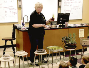 Library class instructor Kay Bivens is seen here giving a talk about Earth Day, Arbor Day and different types of soils and how they sprout seeds differently. She also has a variety of plants on display in front of her.