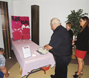 Cindy Welle, center, and Trina Zagar-Brown, right, watch as Dick Welle tries his luck at bra pong, one of the games at the Forks & Flavors fundraiser event for a new 3-D mammography machine for Pioneers Medical Center. The idea is to bounce a ping pong ball off the table and into one of the cups of one of bras against the wall. It is not an easy feat, as most of those who tried the game found out.