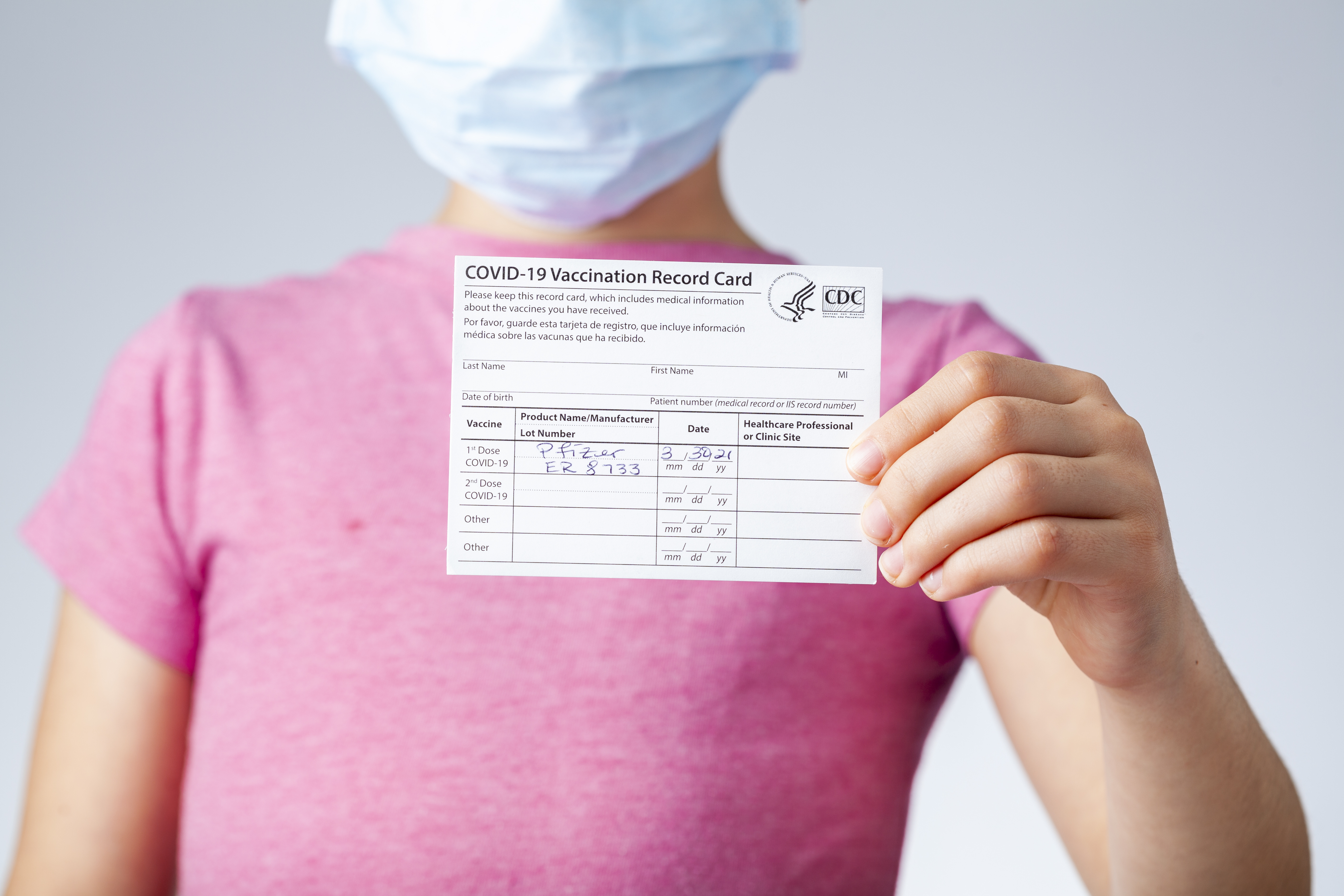 a child in a pink shirt holds up their covid vaccine card